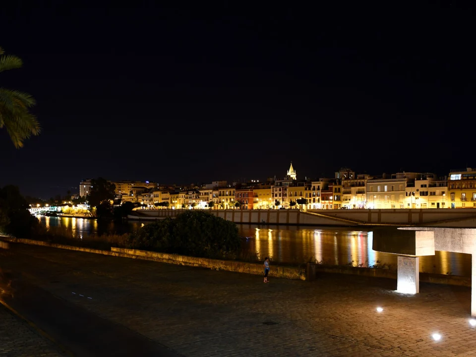La calle Betis de Sevilla de noche vista desde la otra orilla del Guadalquivir, con las fachadas iluminadas reflejadas en el río