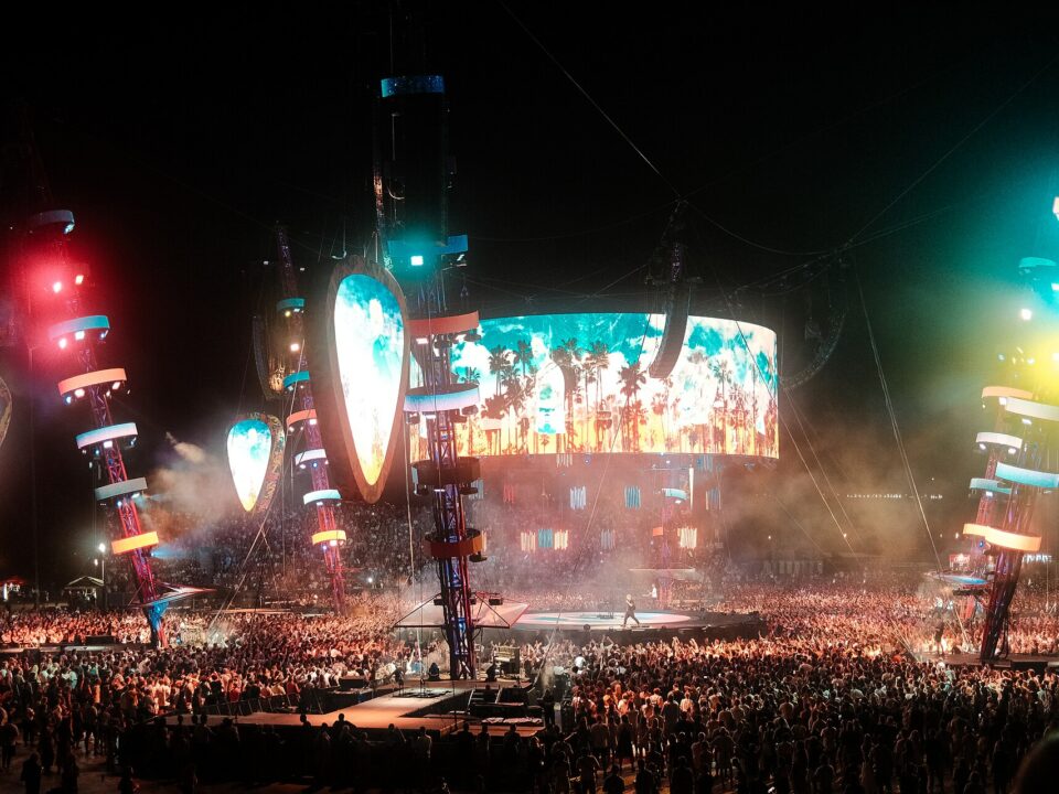 Público en un concierto con las manos en alto bajo focos de colores frente al escenario