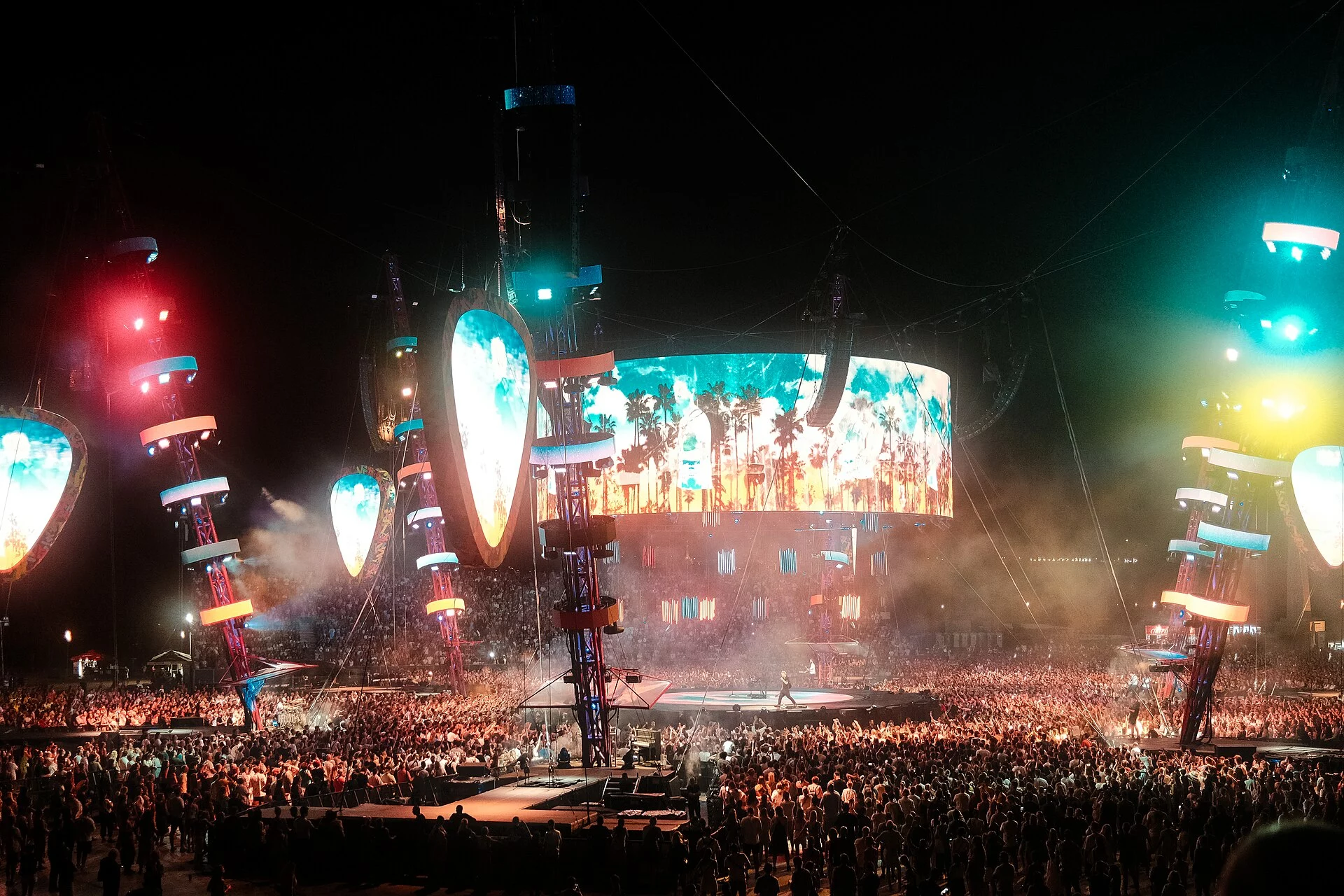 Público en un concierto con las manos en alto bajo focos de colores frente al escenario