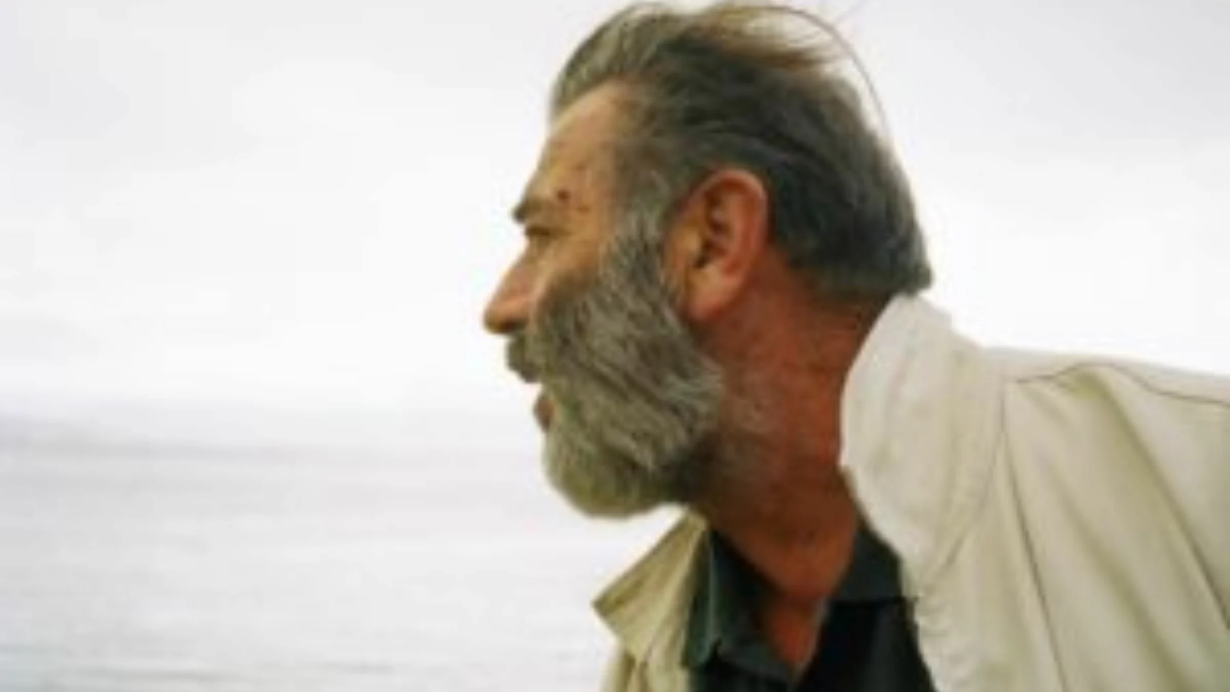 Vari Caramés de perfil, con barba canosa y chaqueta clara, frente al mar en un día gris