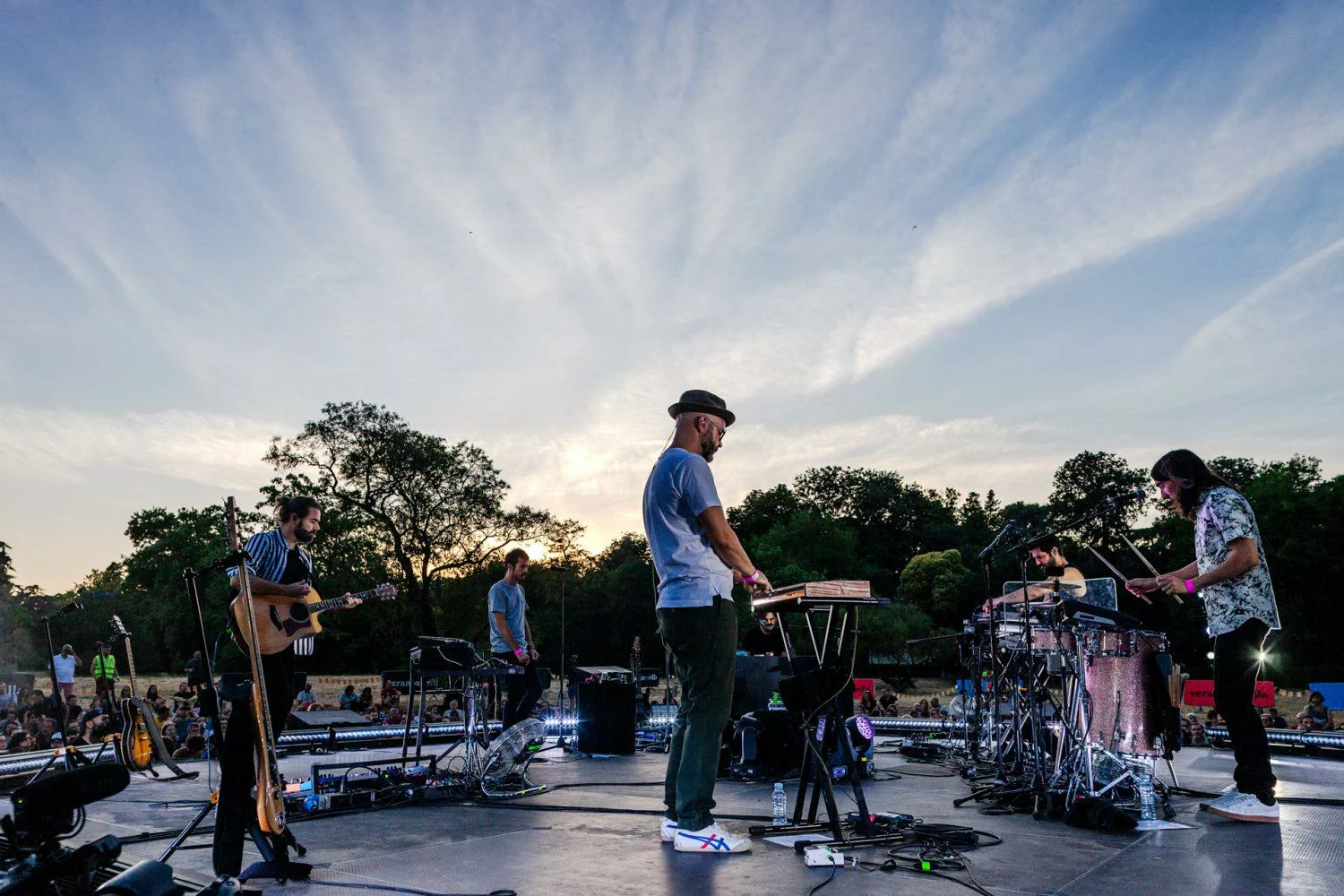 Vetusta Morla en directo en un escenario al aire libre al atardecer, con el público delante